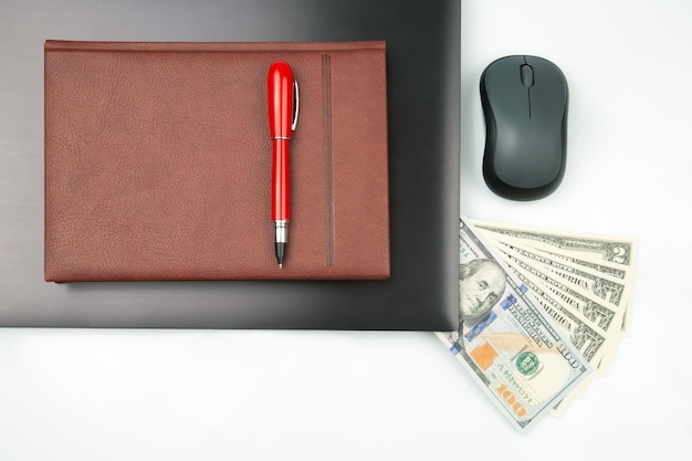 Dollar bills on a white background next to a laptop notepad red pen and computer mouse Online business sale Financial business success