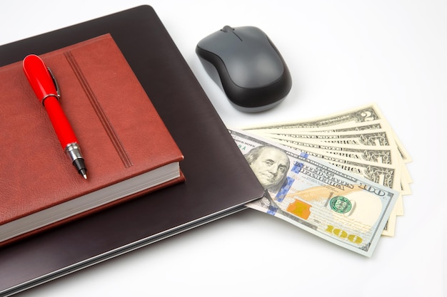 Dollar bills on a white background next to a laptop notepad red pen and computer mouse Online business sale Financial business success