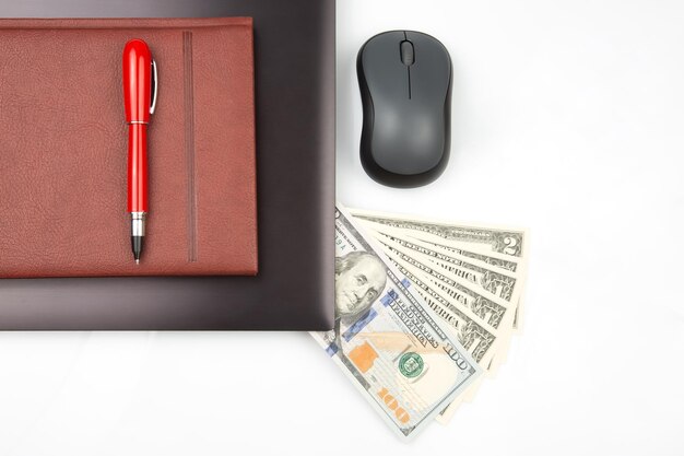 Dollar bills on a white background next to a laptop notepad red pen and computer mouse Online business sale Financial business success