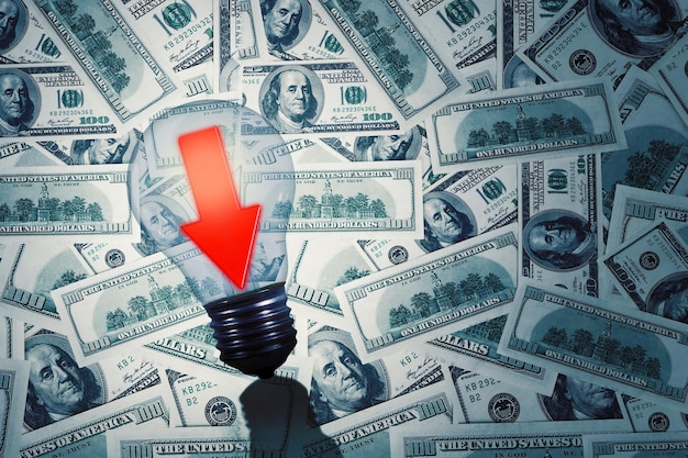 Photo dollar bills with downwards arrow in a light bulb business and recession fears concept
