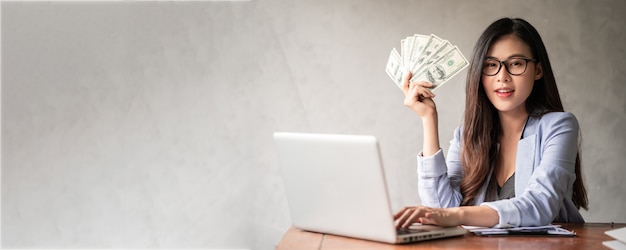 Photo dollar in a businesswoman hand. an asian woman is working from home or office and glad to get dollar money from work and from a supplementary career or part-time self-employment.