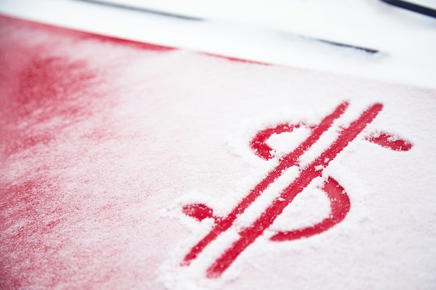 Dollar sign in the snow. Red dollar sign on a snowy car hood. The concept of an accident in bad weather, a large repair cost.