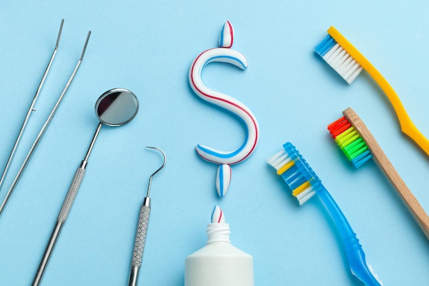 Photo dollar sign of toothpaste tube of colored toothpaste and a toothbrush and dentist tools mirror hook