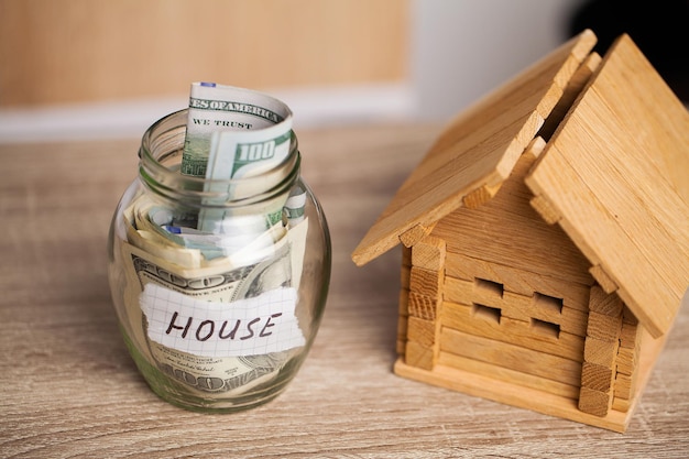 Dollarbiljetten in glazen pot en tekst huis op houten tafel.