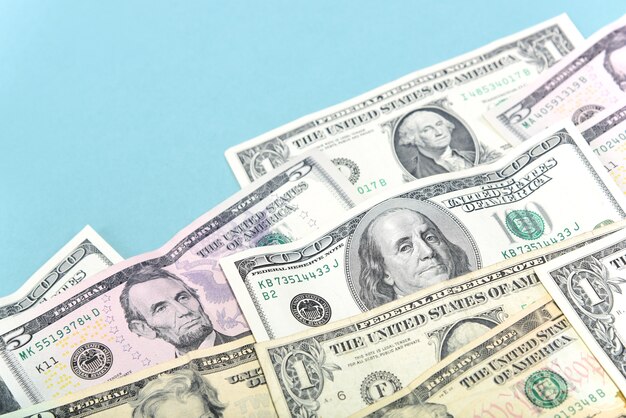 Dollars of different denominations lie on a pale  blue background