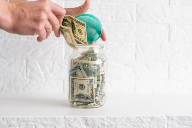 Photo dollars in a glass jar. a view of man's hand putting dollars in the jar bank. a concept of saving money at home.