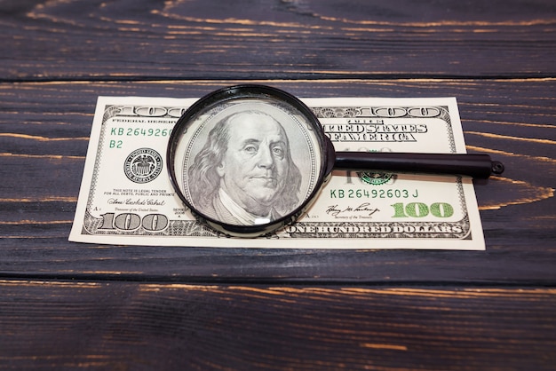 Dollars and a magnifier on a wooden background. View from above.