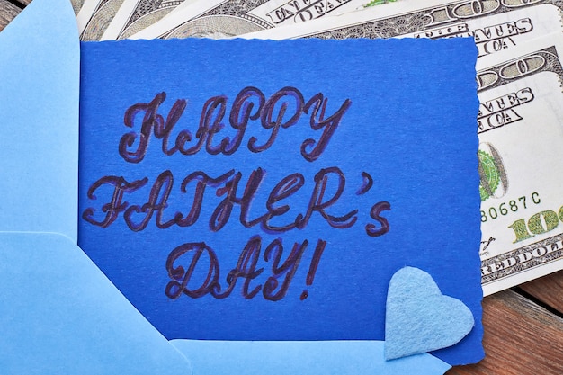 Доллары возле карты День отца. Сердце голубой ткани на карточке. Финансовая поддержка папы.