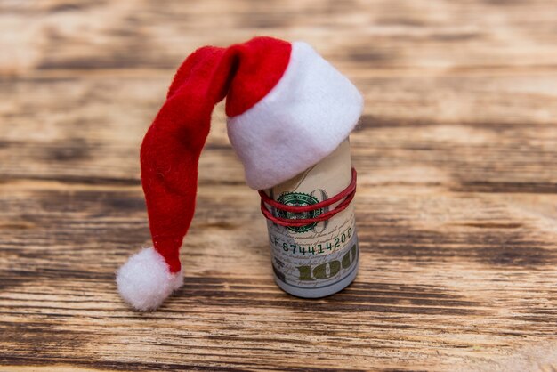 Dollars in roll with santa hat on wooden background