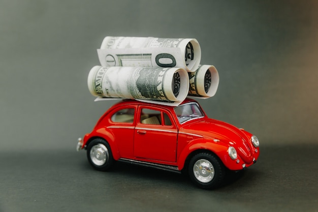 Photo dollars rolled into a tube on the roof of a miniature model car. red car carrying money