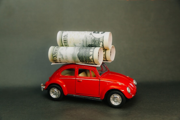 Dollars rolled into a tube on the roof of a miniature model car. red car carrying money