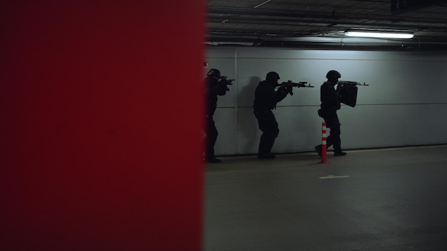 Dolly shot of swat police officers walking on underground parking with weapons special forces aiming assault rifles during military operation anti terrorist squad investigating building at night