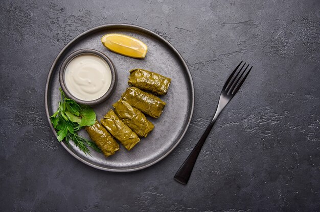 Dolma peterselie steelpan met zure room en citroen in zwarte plaat op donkere tafel in de buurt van zwarte vork top