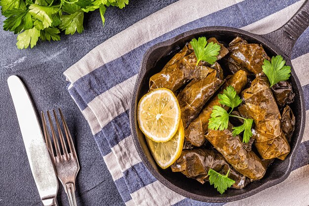 Foto dolma, foglie di vite ripiene con riso e carne su sfondo scuro, vista dall'alto.