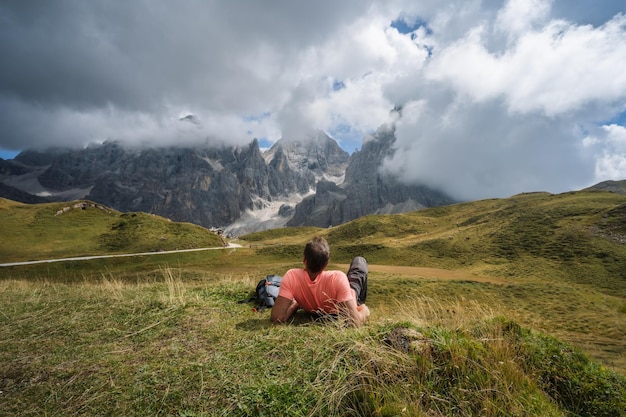 Dolomites Man laying on the grass enjoying Baita Segantini mountain with Cimon della Pala peak