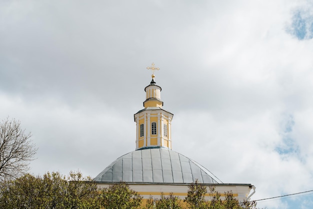 Dome of church with golden cross against cloudy sky, day. Ancient Orthodox monastery or chapel.