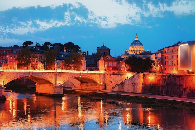 Dome of Saint Peters Basilica in Vatican city and Ponte Sant Angelo Bridge over the Tiber River, in Rome in Italy. It is is also called as the Bridge of Hadrian. Illuminated late in the evening