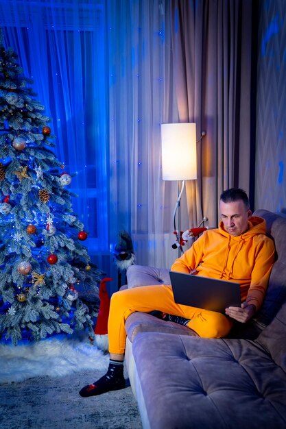 Domestic atmosphere Full length view of the businessman wearing pajama sitting with the laptop near the fur tree