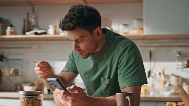 Foto uomo d'affari domestico che guarda lo smartphone al mattino in cucina da vicino uomo che mangia