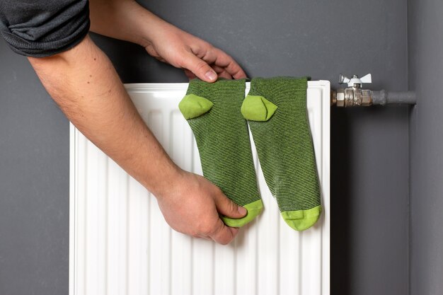 Domestic heating radiator. Man's hand hold socks that dry on radiator.