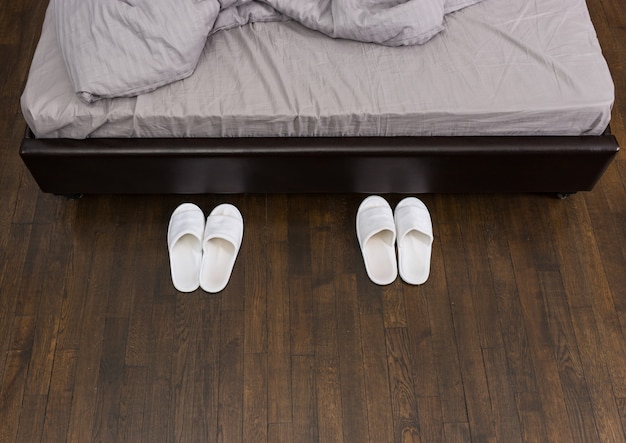 Domestic white slippers are beside the bed in the bedroom in loft style