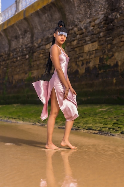 Dominican ethnic girl with braids with a beautiful pink dress. Fashion enjoying the summer walking on the beach