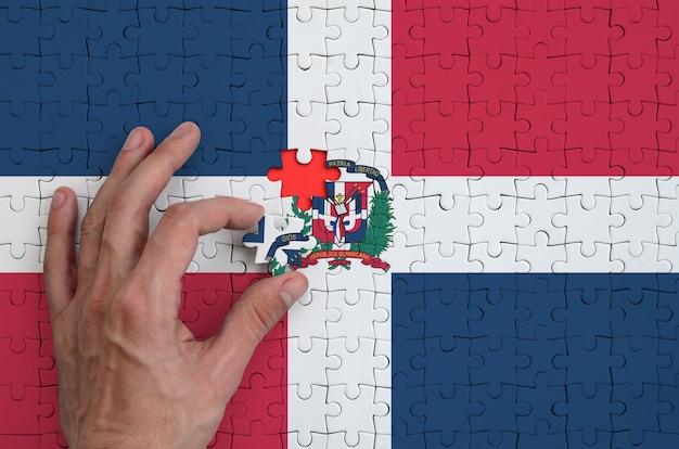 La bandiera della repubblica dominicana è raffigurata su un puzzle che la mano dell'uomo completa per piegare