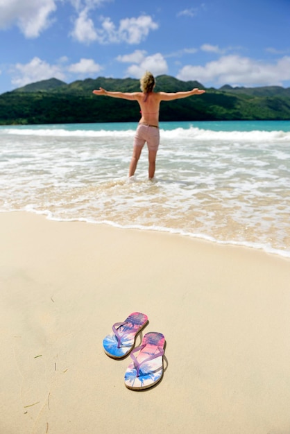 Dominican Republic, Samana, flip-flops on the beach and woman in the sea
