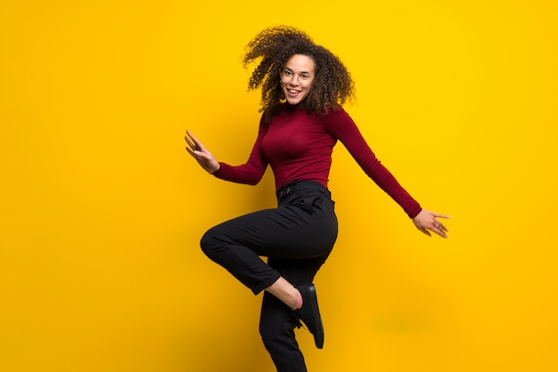 Dominican woman with curly hair jumping over isolated yellow wall