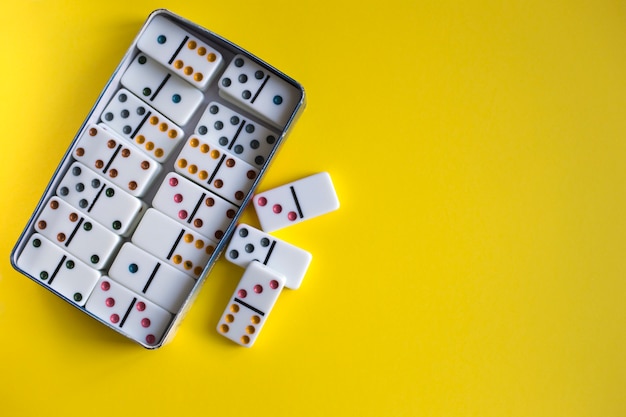 Domino game in metal box on yellow background, top view. family
board game