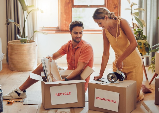 自宅で機器を梱包するために一緒に働く若いカップルの梱包と箱を寄付する リサイクルのために家を整理する男女の関係の一体感とチームワーク