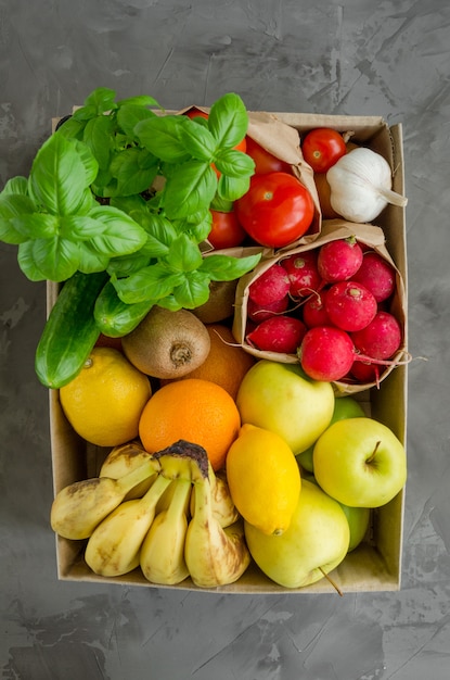 Donatie box met verse biologische groenten, fruit en kruiden op een concrete achtergrond. goede voeding. bezorg gezond voedsel aan huis.