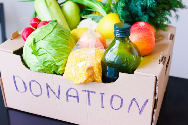 Foto donatie van voedsel. doos met fruit en groenten appels kool radijs courgette olie, grutten close-up.