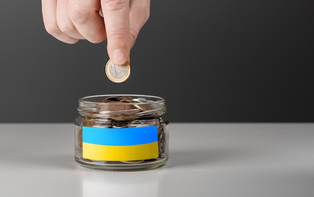 Donatie voor Oekraïense vluchtelingen Hulp en financiële hulp aan Oekraïne donatiepot met Oekraïense vlag Oekraïense oorlogsdonaties Hand munten in glazen pot zetten