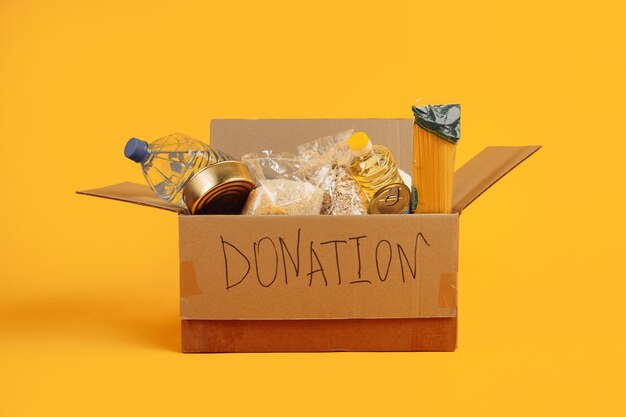 Donation box. open cardboard box with clothes and food on a\
yellow background.