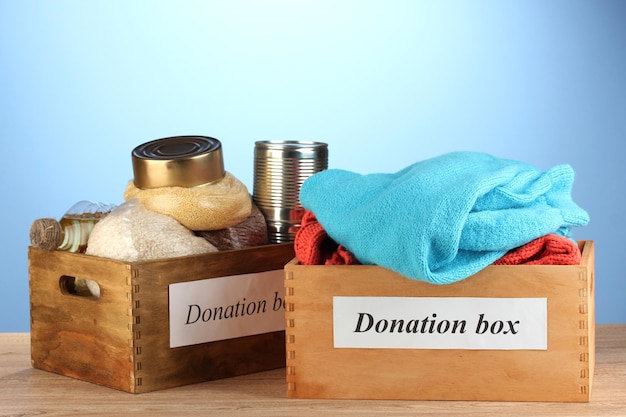 Donation boxes with clothing and food on blue background closeup