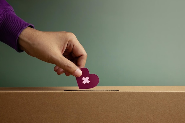 Photo donation concept hand drop a paper heart with cross into a donate box helping supporting and togetherness side view