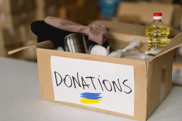 Фото Пожертвование еды для беженцев из украины поддержка жертв войны помощь людям благотворительная коробка с украинским флагомконцепция гуманитарной помощи