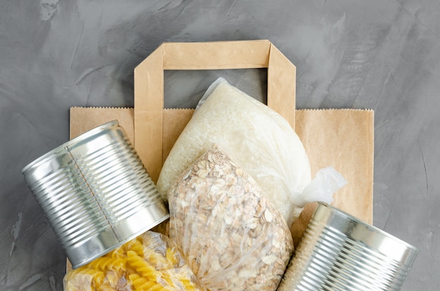 Donation food. Paper bag with canned food, pasta, oatmeal, rice and toilet paper on a dark concrete background. Food delivery.