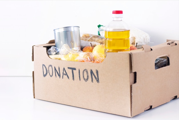 기부. 식료품 상자, 그것을 필요로하는 사람들을위한 제품을 도와주십시오. 기부금 상자. 흰색 표면에 음식 비문 기부와 골 판지 상자.