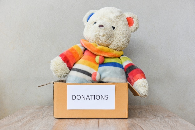 Donations box with teddy bear doll wooden table background