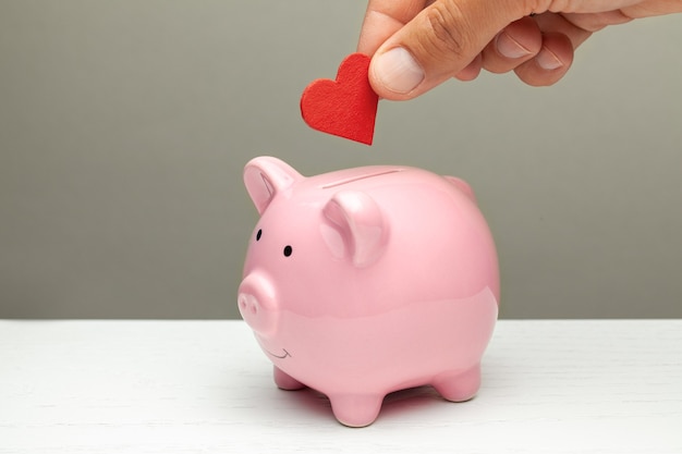 Donations of love and feelings, sympathy. Man puts heart in piggy bank.