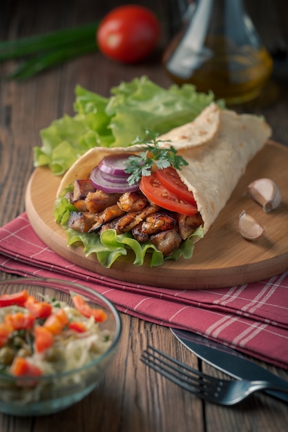 Doner kebab is lying on the cutting board. Shawarma with chicken meat, onions, salad lies on a dark old wooden table.