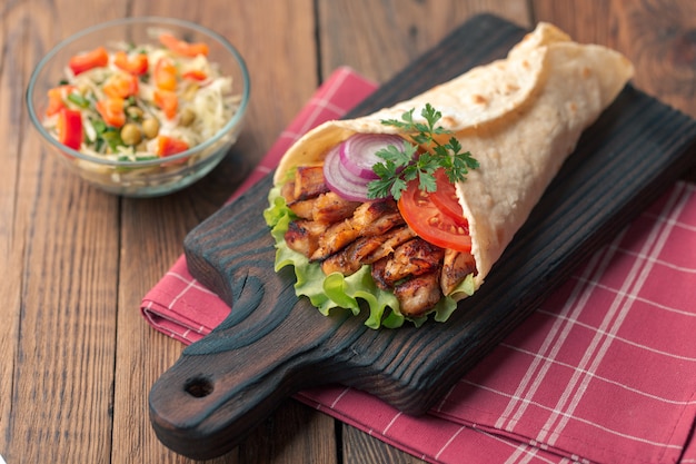 Il kebab di doner giace sul tagliere. shawarma con carne di pollo, cipolle, insalata si trova su un vecchio tavolo di legno scuro.