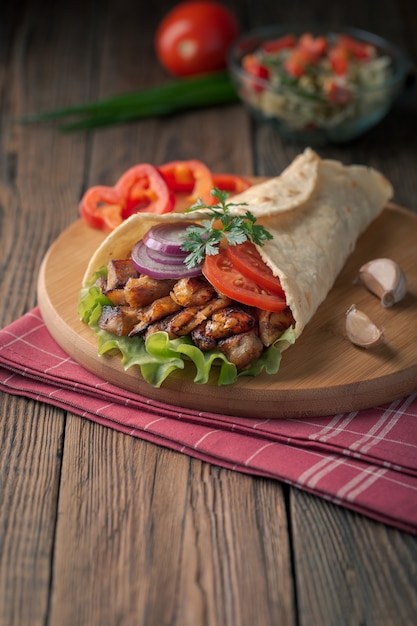 Doner kebab ligt op de snijplank. Shoarma met kippenvlees, uien, salade ligt op een donkere oude houten tafel.