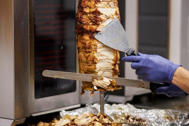 Foto carne di doner kebab. lo chef prepara il doner kebab. shawarma o giroscopi su uno spiedino di metallo. donatore di cottura