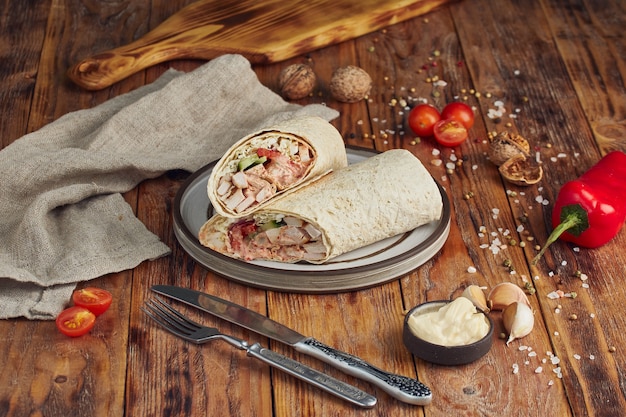 Doner kebab (shawarma or doner wrap). Grilled chicken on lavash with tomatoes, green salad and peppers on the wooden table