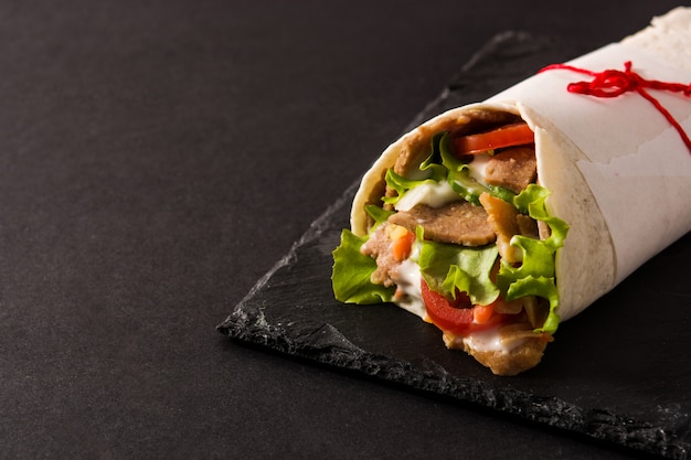 Doner kebab or shawarma sandwich on black slate surface copy space