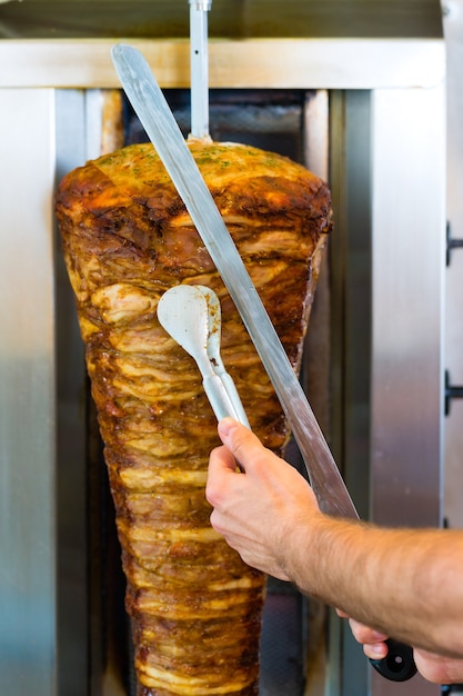 Döner kebab - vriendelijke verkoper in een Turks fastfoodrestaurant, vlees snijden met een scherp mes voor een spies