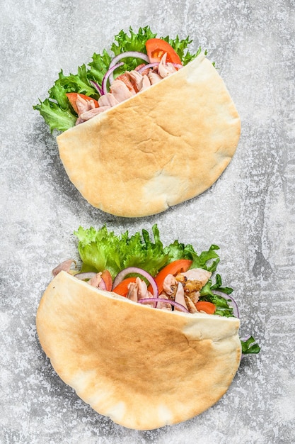 Doner kebab with grilled chicken meat and vegetables in pita bread on gray. Top view.